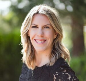 Image of Lauren Erickson; smiling white woman with blonde shoulder-length hair, wearing a black top with lace sleeves